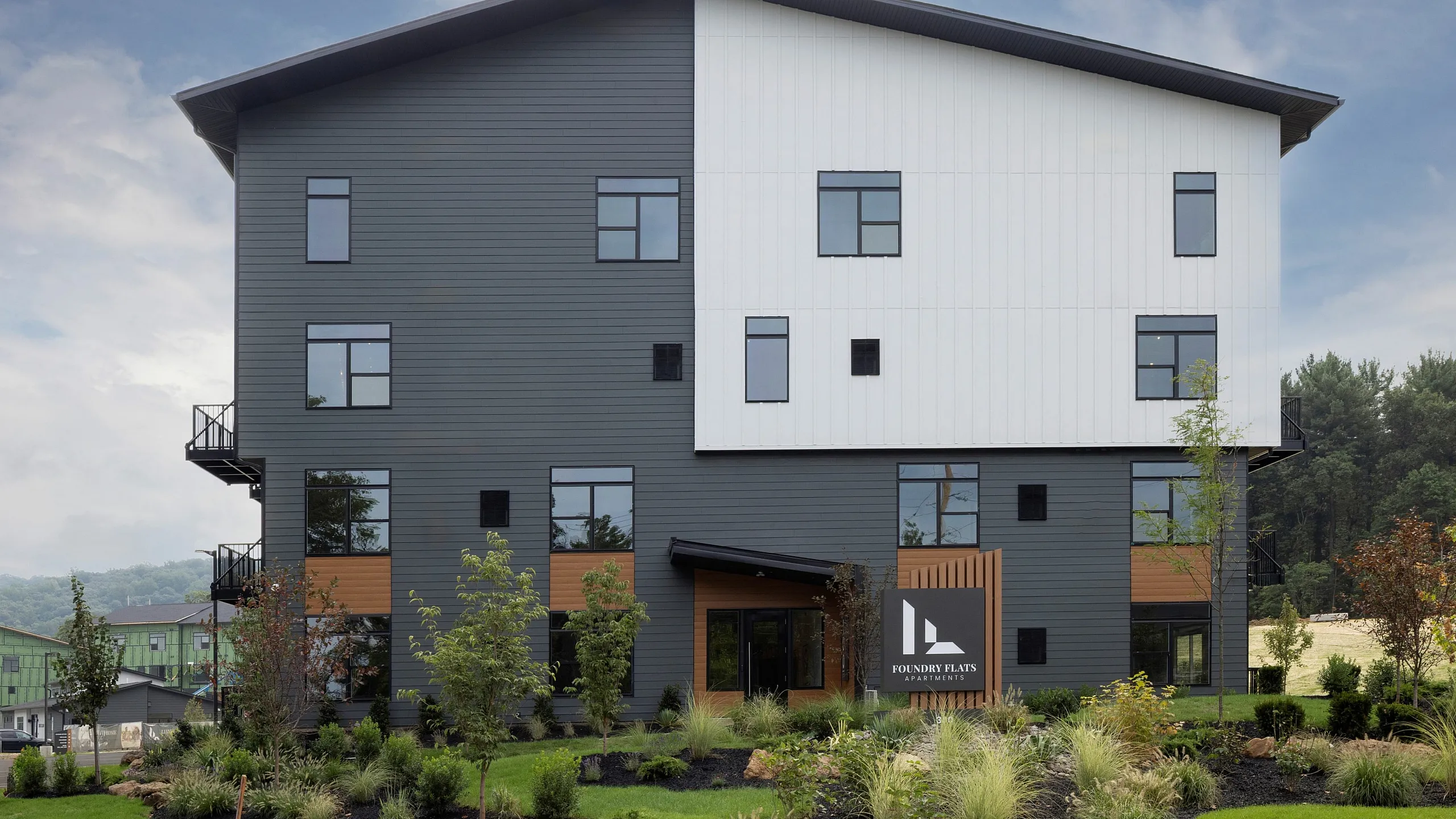 Modern residential building with sleek design, lush landscaping, and spacious windows under a bright sky, located in a scenic area.