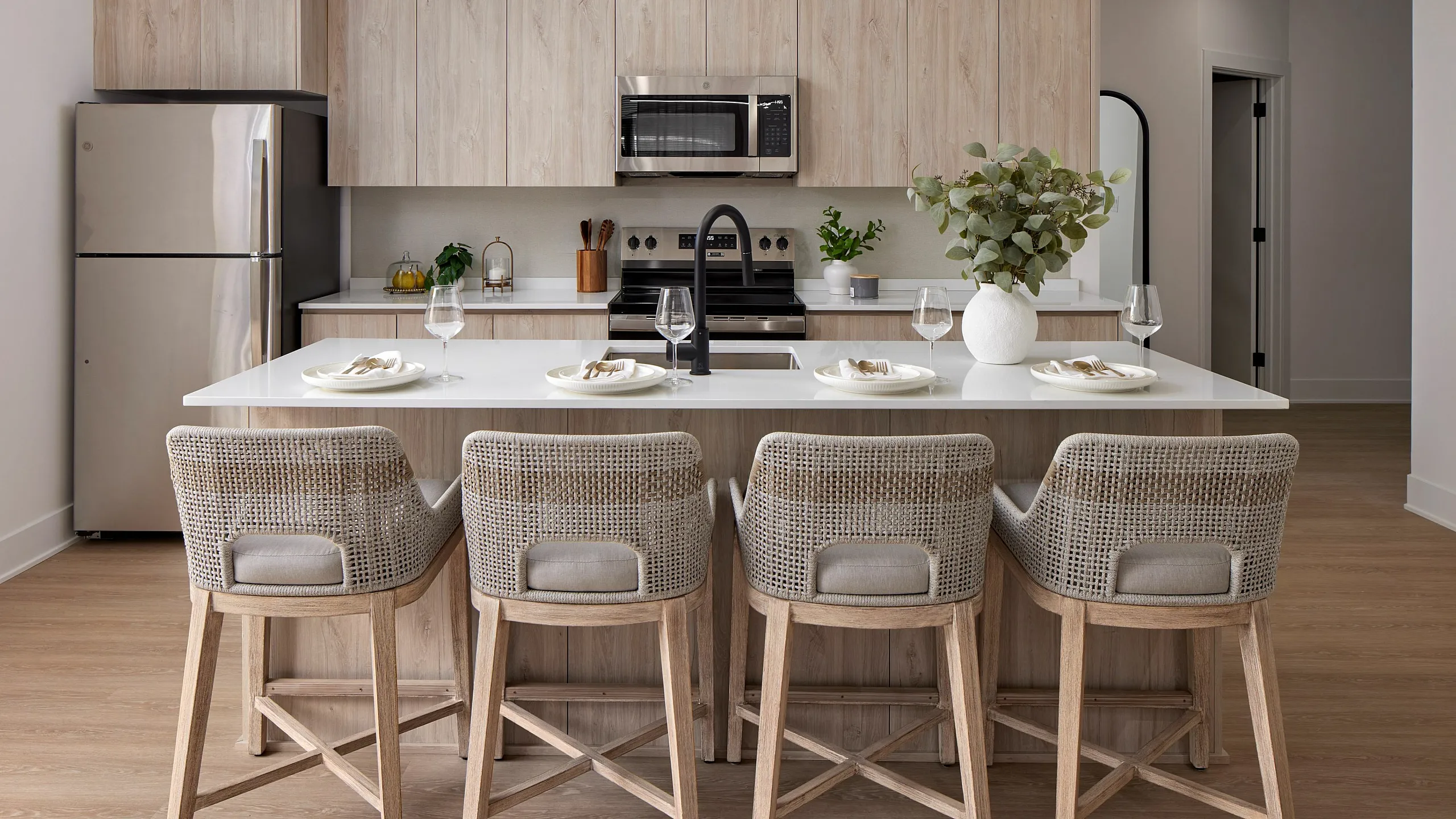 Modern kitchen with sleek wooden cabinetry, stainless steel appliances, and a stylish island bar with wicker chairs.