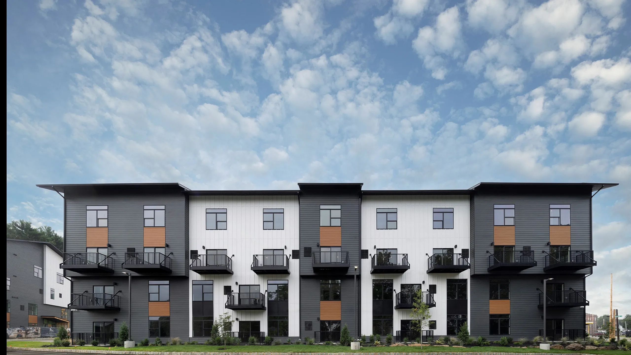 Contemporary apartment building with modern facade, spacious balconies, and ample parking, set against a clear blue sky.