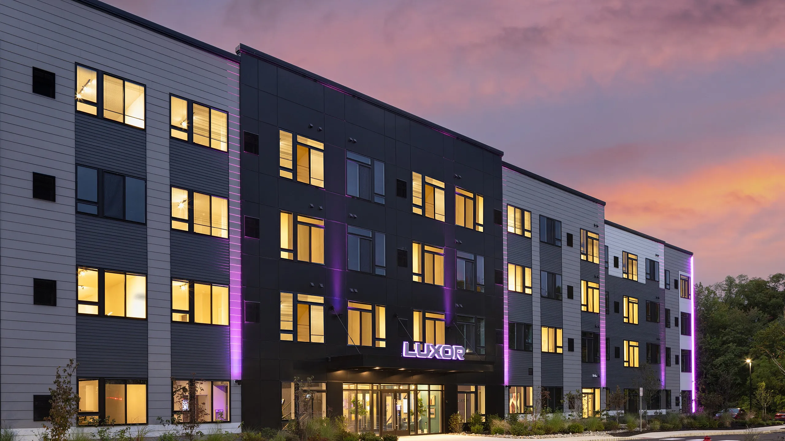 Modern apartment building with illuminated windows and sleek black and white facade, set against a stunning sunset sky.