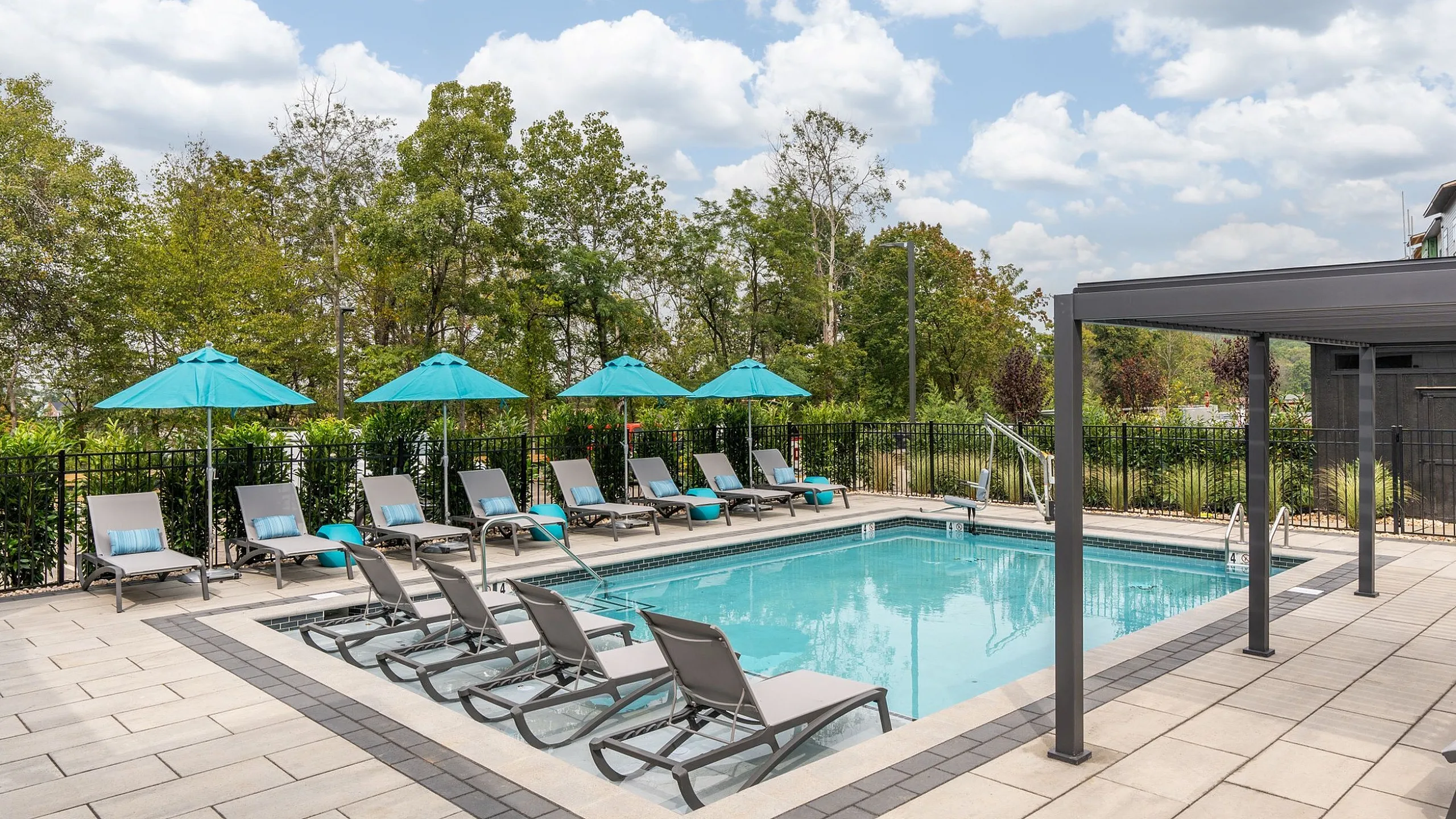 Inviting outdoor pool area with modern lounge chairs and vibrant umbrellas, surrounded by lush greenery for a tranquil retreat.