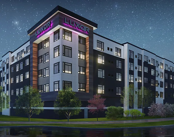 Luxurious modern apartment building illuminated at night, showcasing sleek architecture and vibrant lighting in a serene neighborhood setting.