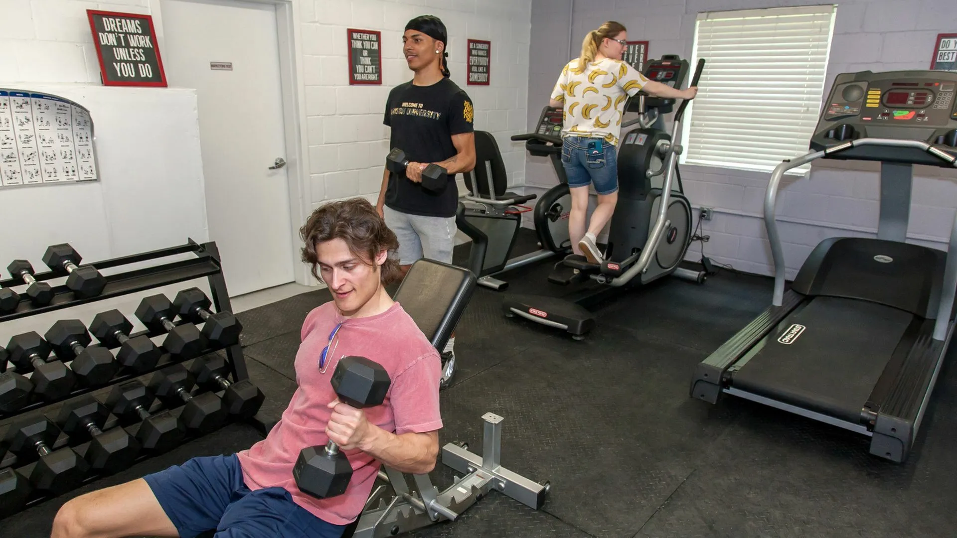 Inviting gym with diverse equipment and people working out, featuring weights and cardio machines.