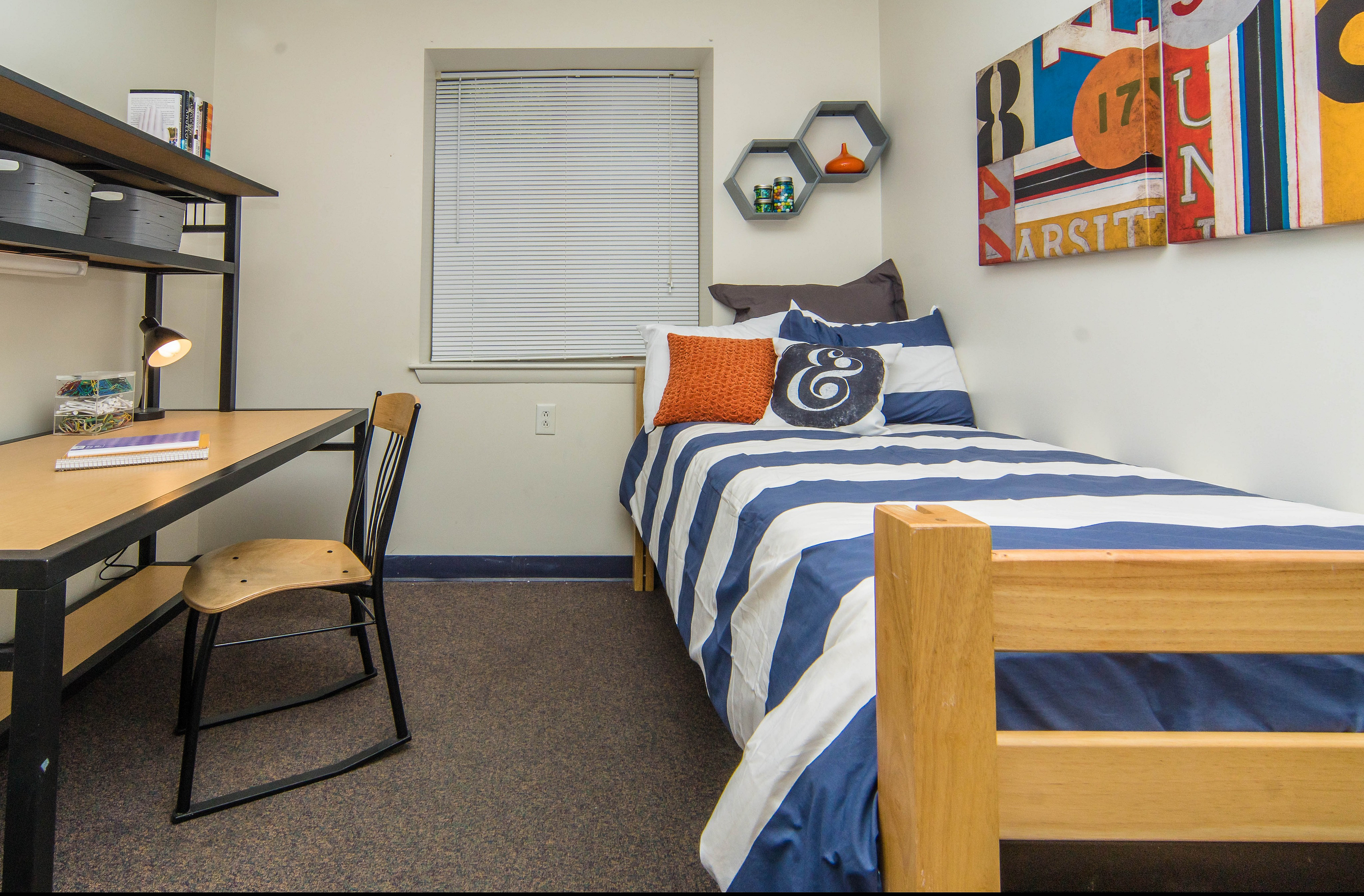 Inviting bedroom with striped bedding, a functional desk, and contemporary wall art, perfect for relaxation and study.
