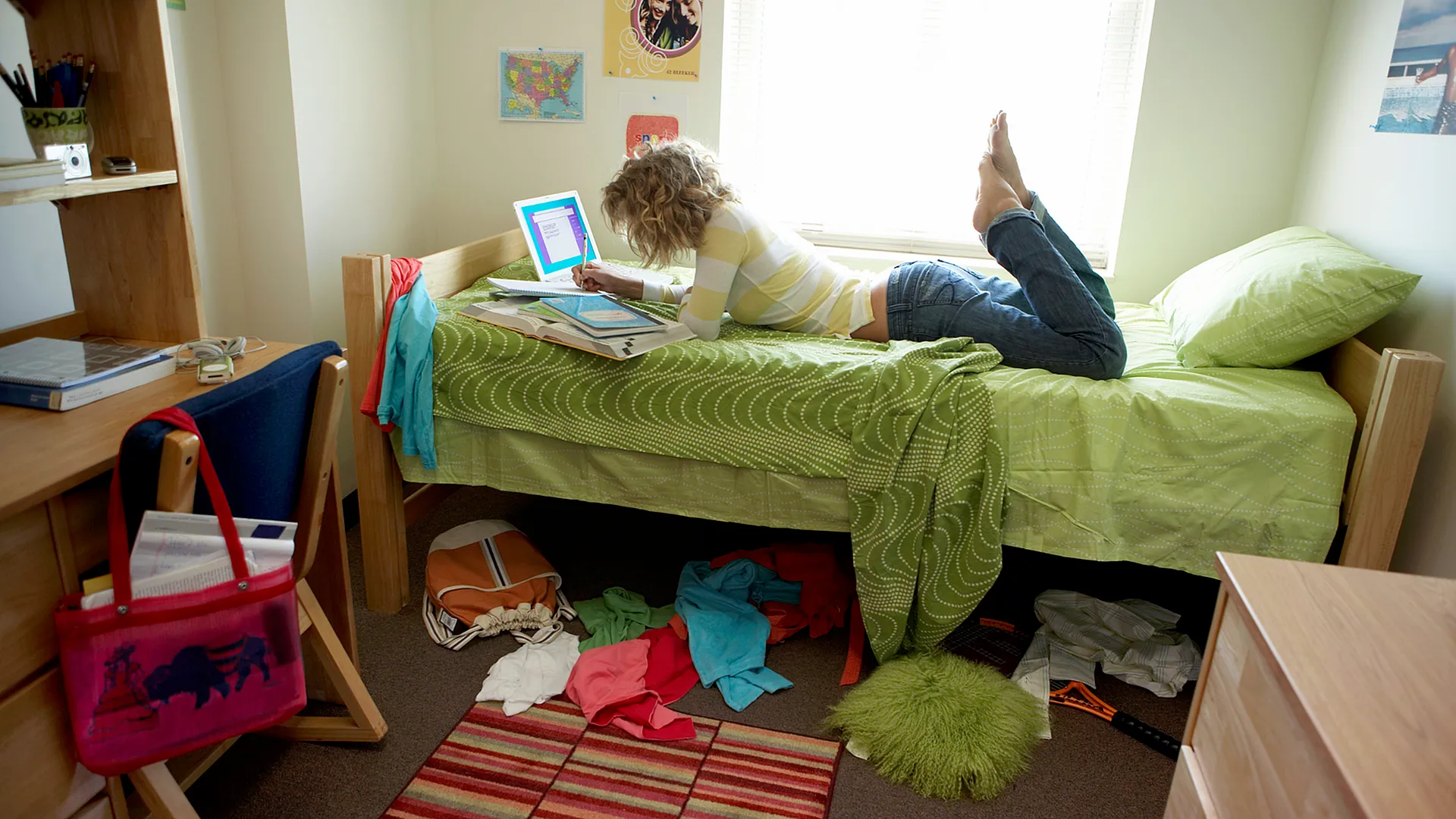 Inviting bedroom with a neatly arranged workspace and vibrant decor, featuring a person relaxing on the bed.