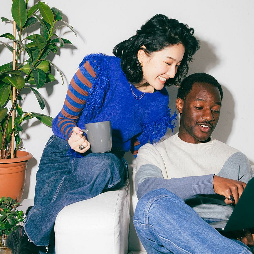 Cozy living room scene with two friends enjoying a laptop on a white couch beside vibrant houseplants.