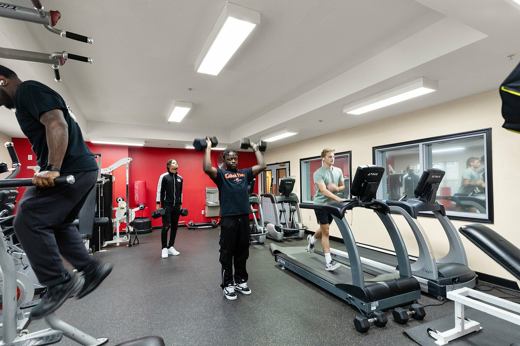 Spacious gym with state-of-the-art equipment, featuring energetic individuals using treadmills and weights, surrounded by a vibrant atmosphere.