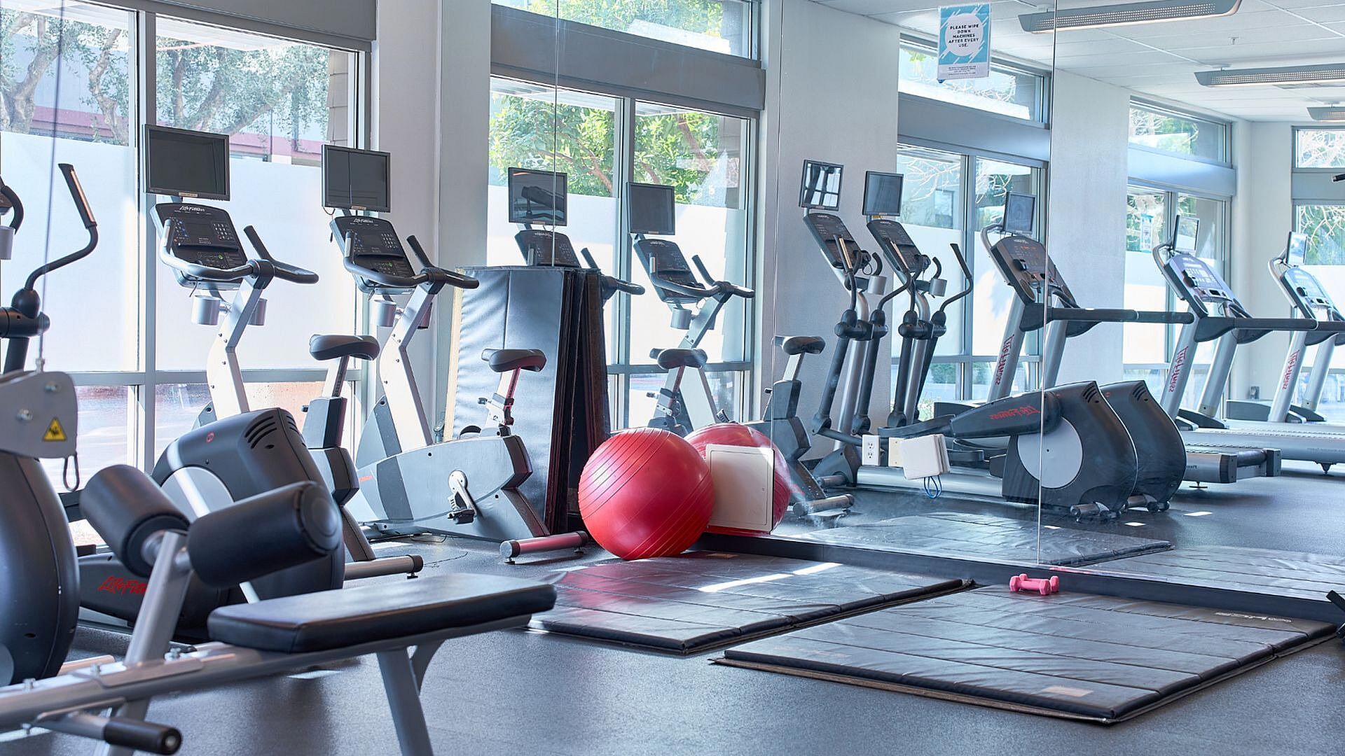 Spacious modern gym with large windows, equipped with top-of-the-line treadmills, cycling machines, and fitness accessories for an invigorating workout.