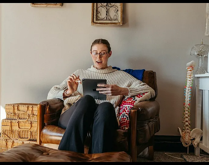 A person relaxing in a cozy living room with a tablet, surrounded by warm decor and wicker baskets.