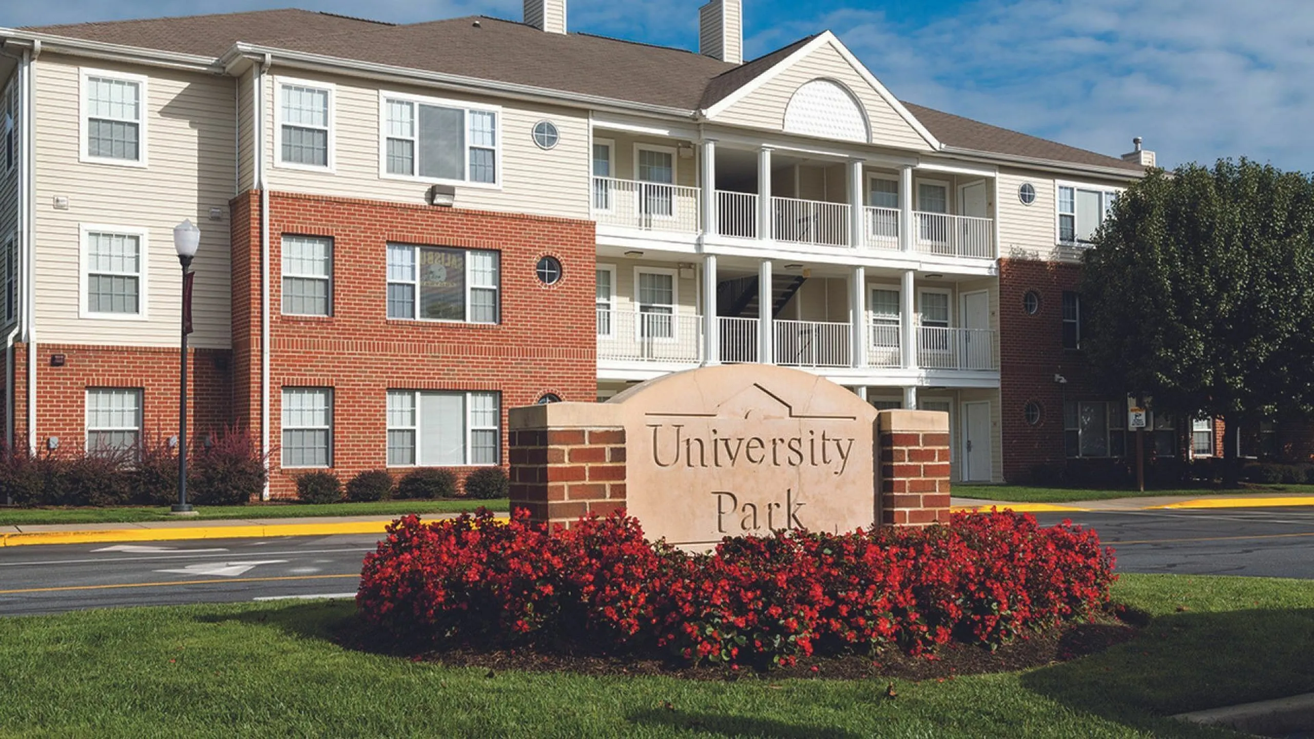 Elegant facade of the University Park apartment complex with well-maintained gardens and vibrant red flowers.