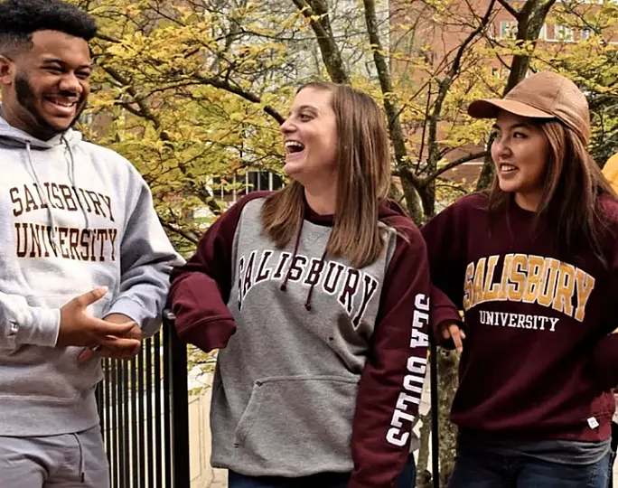 Three students in Salisbury University hoodies laughing outdoors on campus.