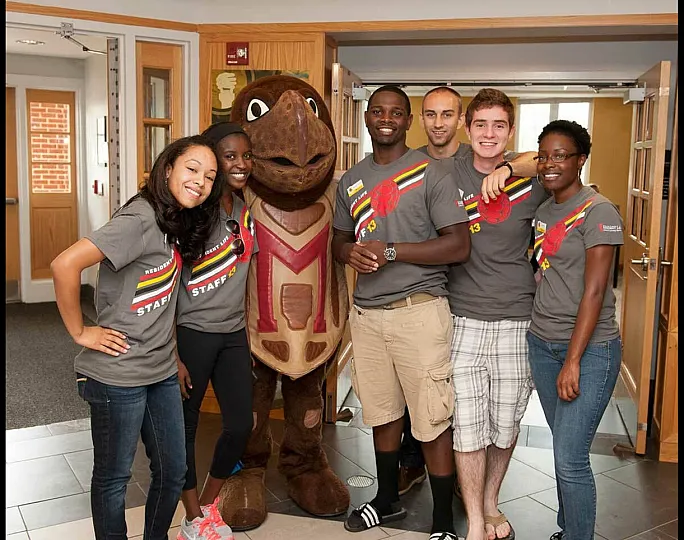 Cheerful group of six people and a mascot in an indoor setting, wearing matching staff t-shirts.