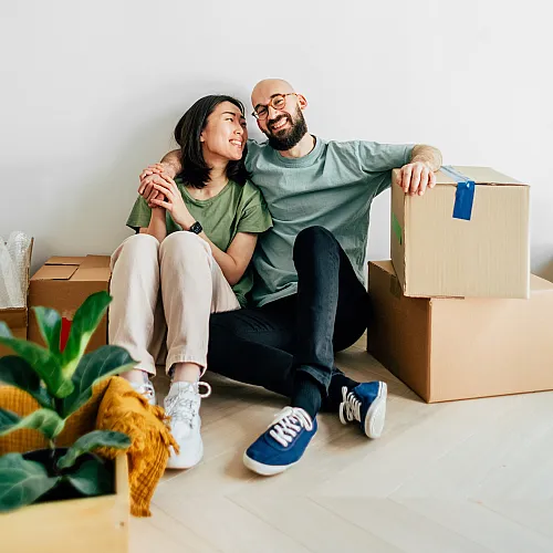 Joyful couple sitting on the floor, surrounded by moving boxes, in a bright home.