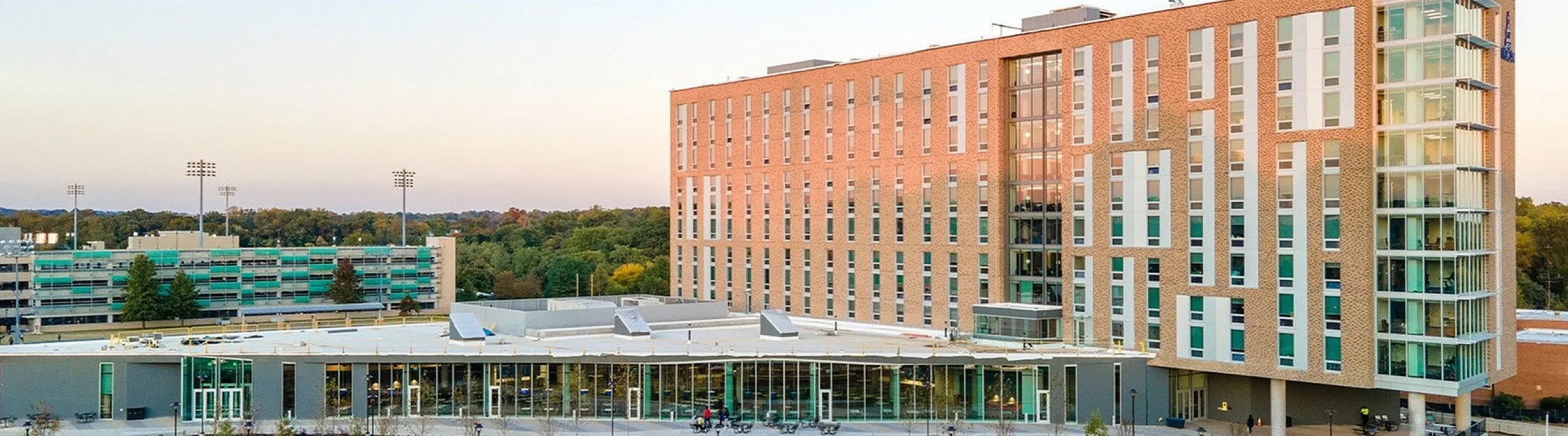Modern apartment complex with sleek architecture, large windows, and a beautifully landscaped exterior, set against a clear evening sky.