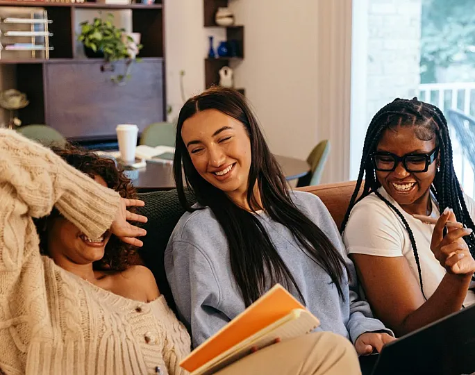 A cozy living room with three friends enjoying a laugh on a comfortable couch, surrounded by books and greenery.