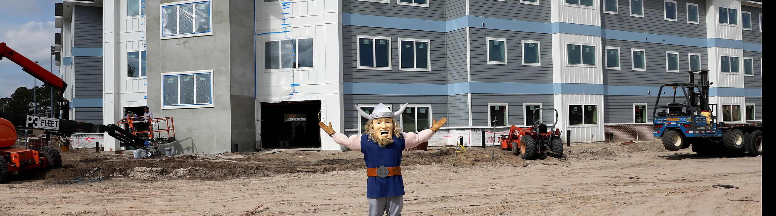 Newly constructed modern apartment complex with sleek design and ample natural light, featuring a cheerful mascot in front for a welcoming atmosphere.
