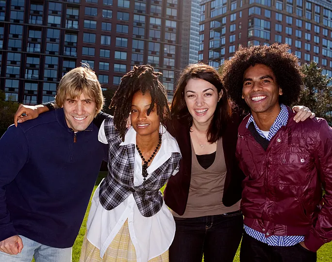 Vibrant city living captured with a group of friends smiling in front of modern apartment buildings against a sunny backdrop.