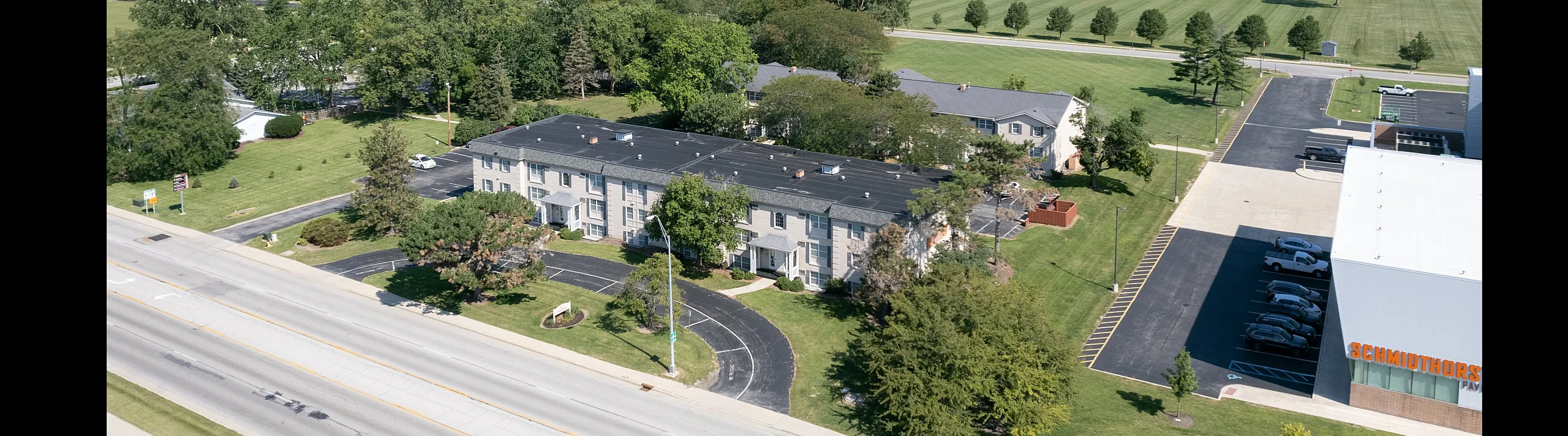 Aerial view of a charming apartment complex surrounded by lush greenery and open spaces, offering a tranquil suburban setting ideal for comfortable living.