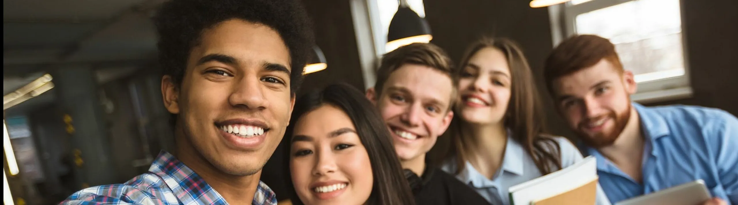 Group of cheerful young adults taking a selfie in a modern, well-lit office environment.