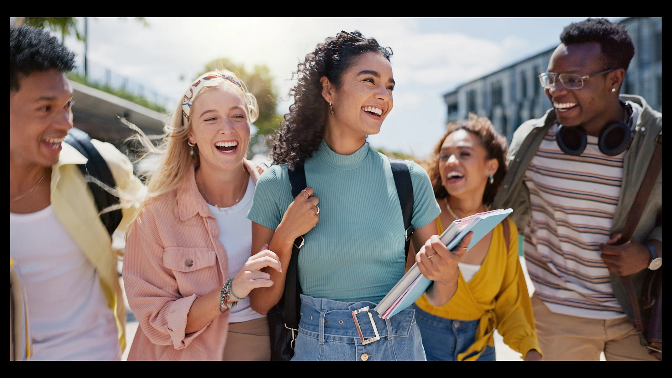 Joyful group of diverse friends laughing and walking outside on a sunny day, exuding happiness and camaraderie.