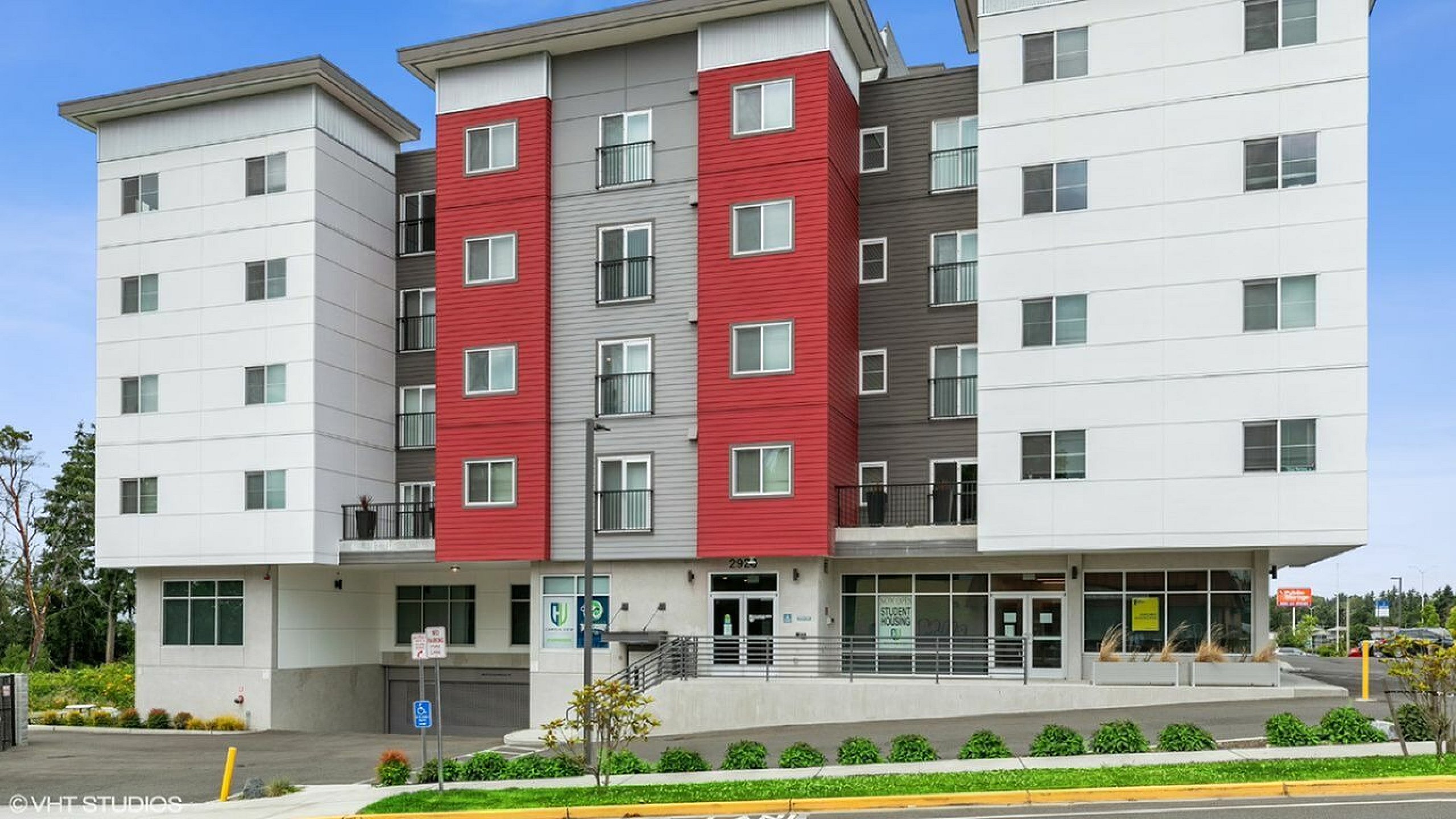 Modern apartment building with colorful accents, featuring spacious balconies and a welcoming entrance, set against a clear blue sky.