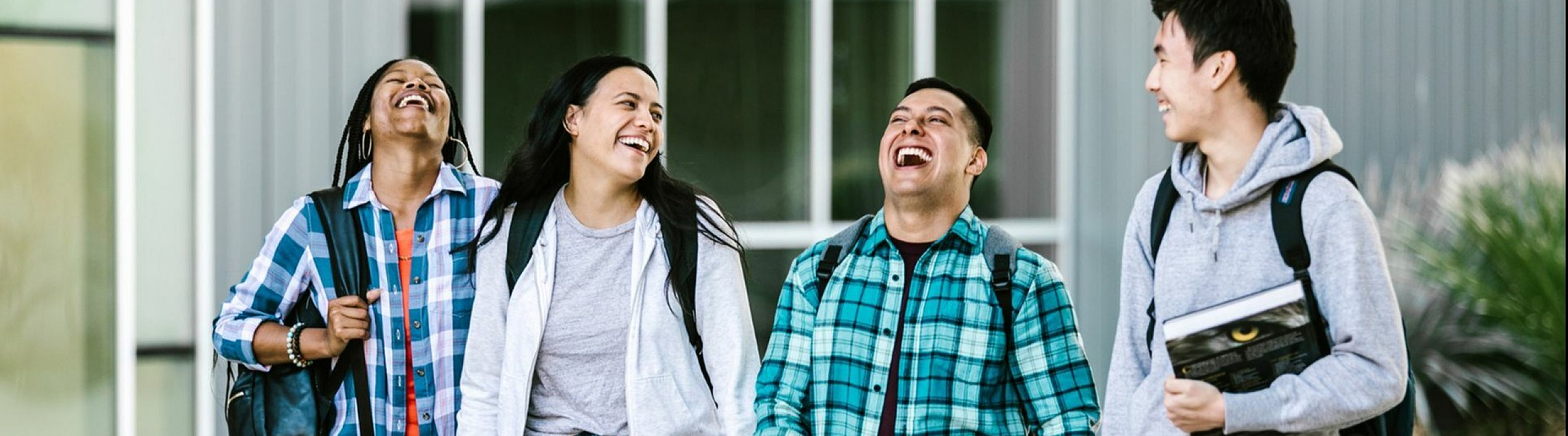 Group of four students joyfully walking together on campus with backpacks and books, sharing a moment of laughter and camaraderie.