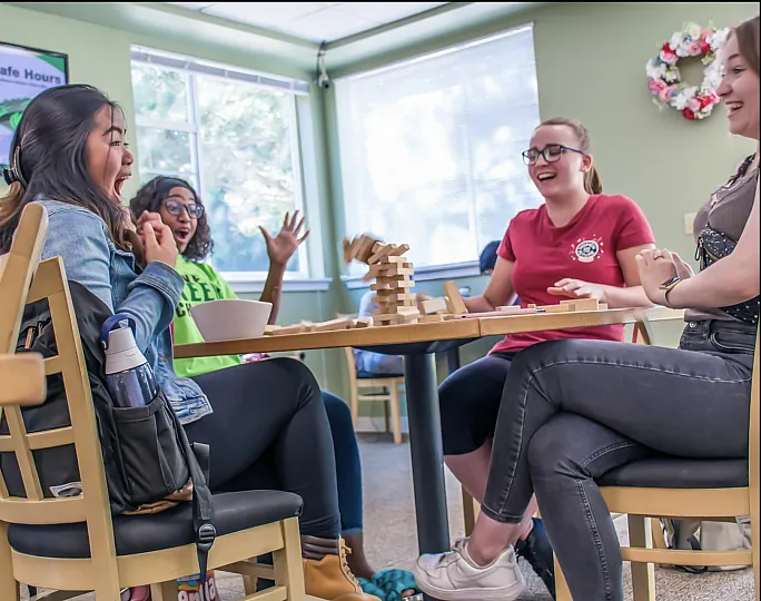 Group of friends laughing and enjoying a game of Jenga at a vibrant cafe setting.