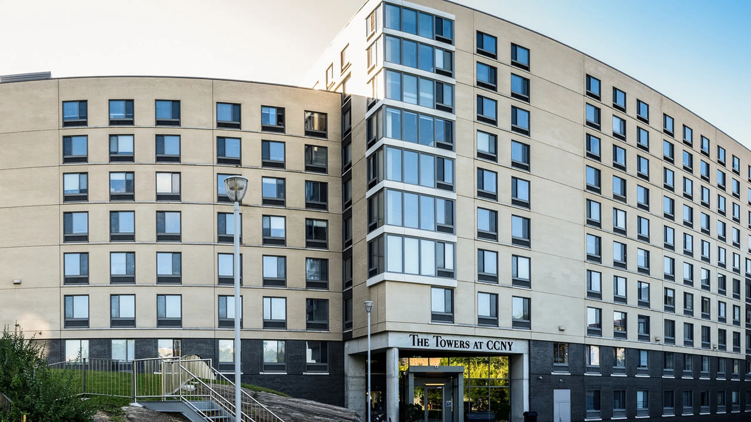 Contemporary apartment building with large windows, lush greenery, and welcoming entrance at The Towers.