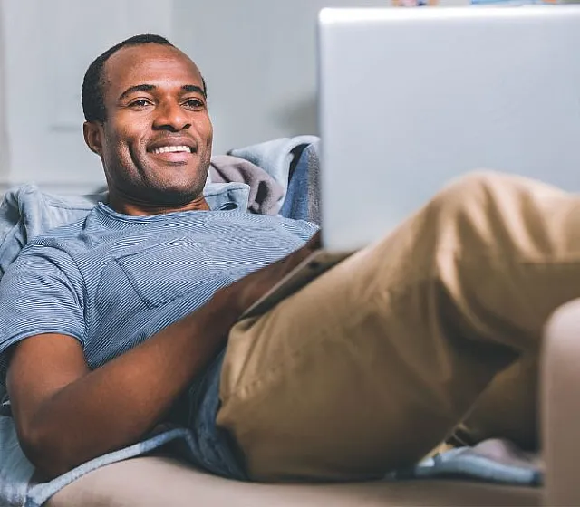 Content man relaxing on a comfortable sofa, engaging with a laptop in a cozy living room setting.
