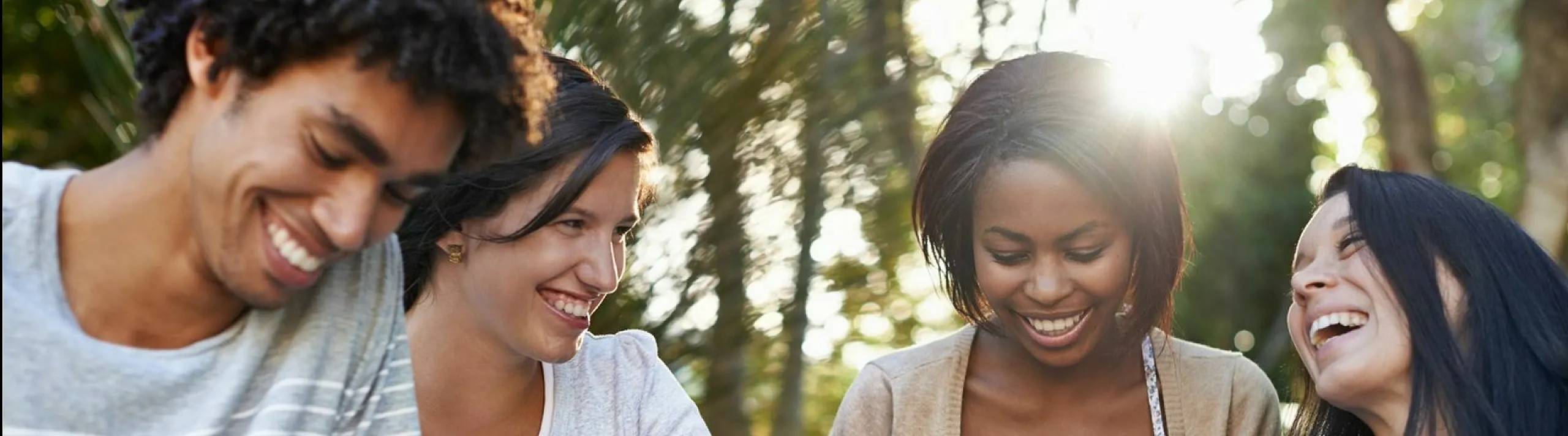 Group of friends enjoying a sunny day outdoors, smiling and sharing moments with digital devices.