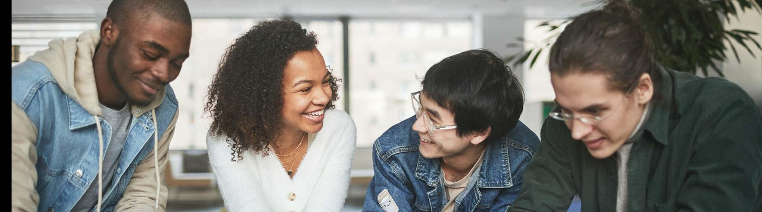Diverse group of smiling friends collaborating in a cozy, sunlit living room, showcasing a vibrant and inclusive atmosphere.