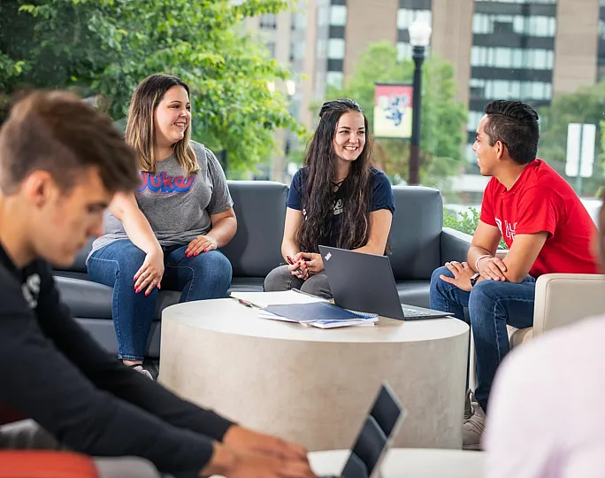 Vibrant student gathering in modern lounge with greenery view, enhancing community spirit and collaboration.