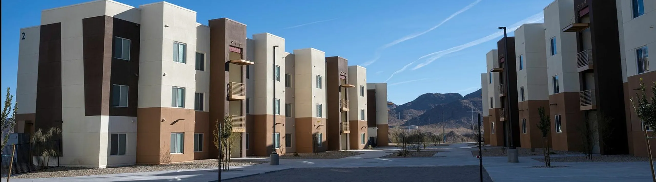Modern apartment complex with mountain views, featuring sleek architecture and spacious surroundings under a clear blue sky.