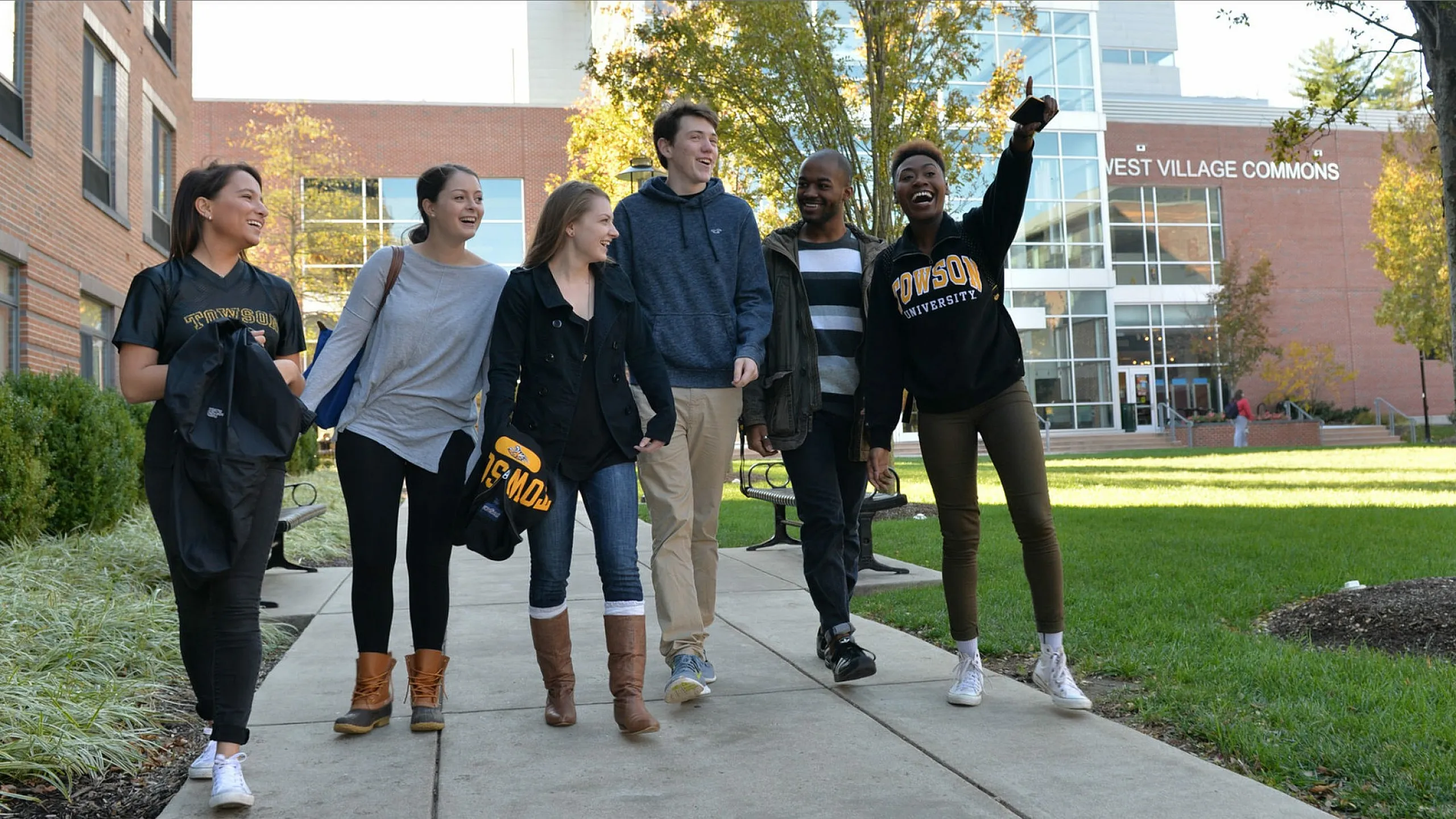 Vibrant group of students joyfully walking together on a sunny campus pathway, surrounded by lush greenery and modern buildings.