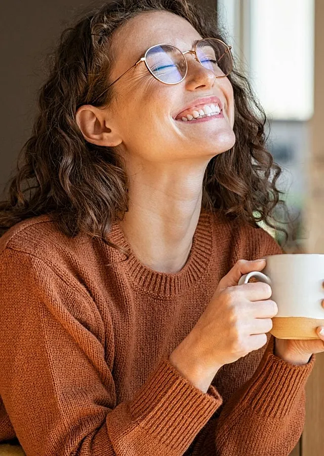 Joyful person enjoying a cozy moment, sipping a warm drink in a stylish, sunlit living space.