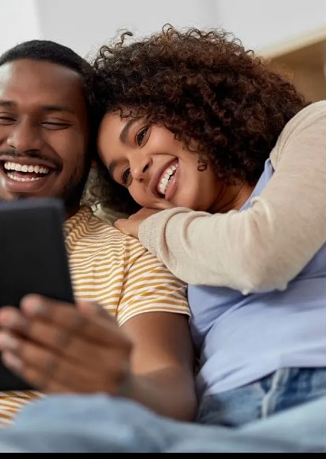Happy couple enjoying cozy living space while browsing on a tablet, embodying comfort and relaxation.