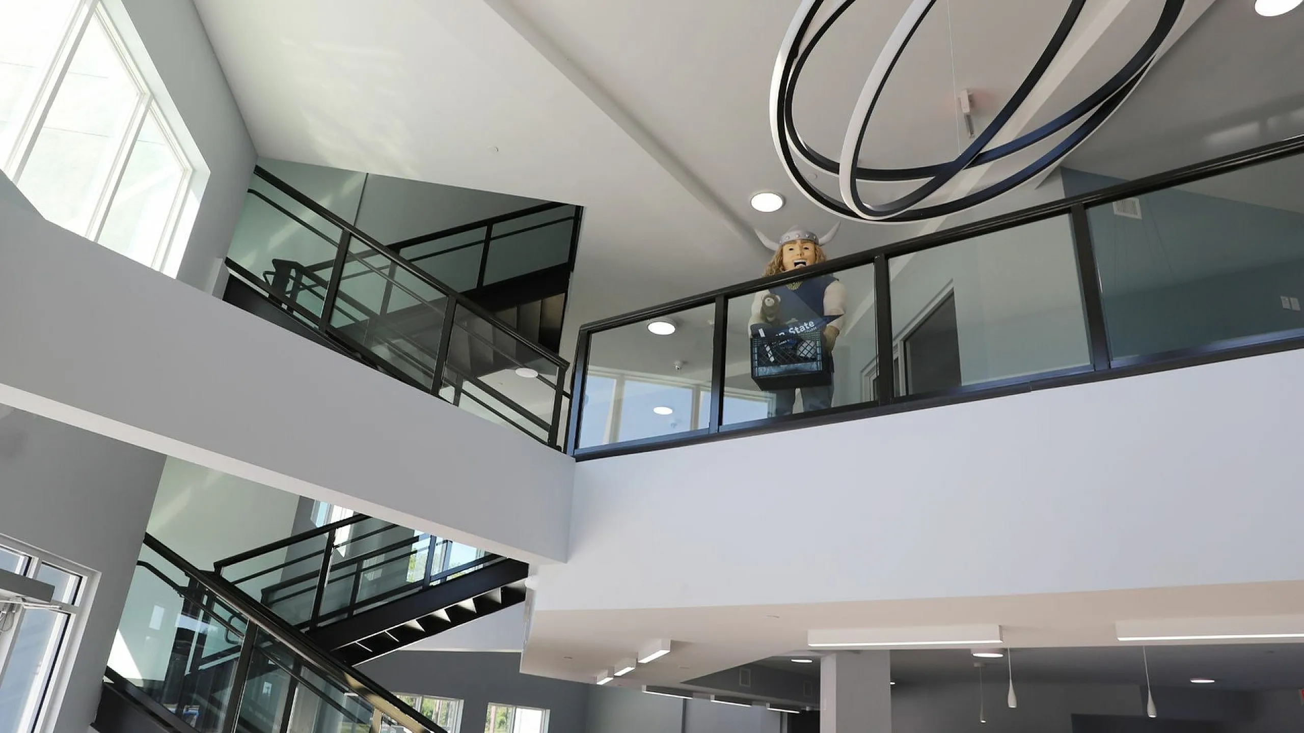 Modern apartment lobby with sleek glass railings, ample natural light, and a unique spiral chandelier.