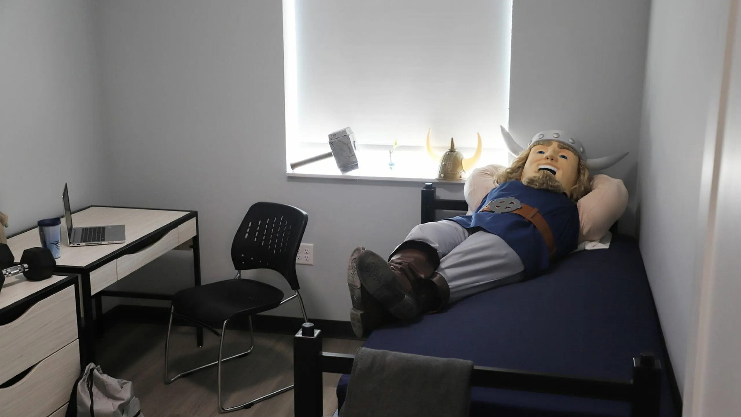 Cozy bedroom with modern desk setup, complete with a charming mascot figure relaxing on the bed, enhanced by playful Nordic decor accents.