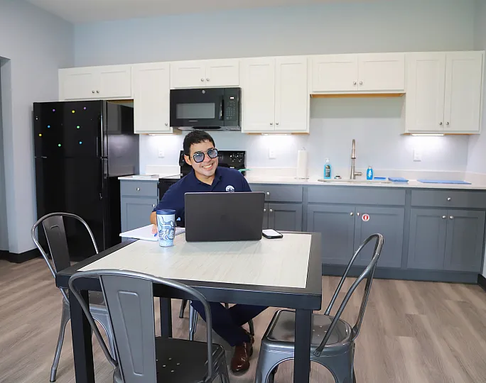 Modern kitchen with sleek cabinetry and stainless steel accents, featuring a relaxed person enjoying a workspace setup.