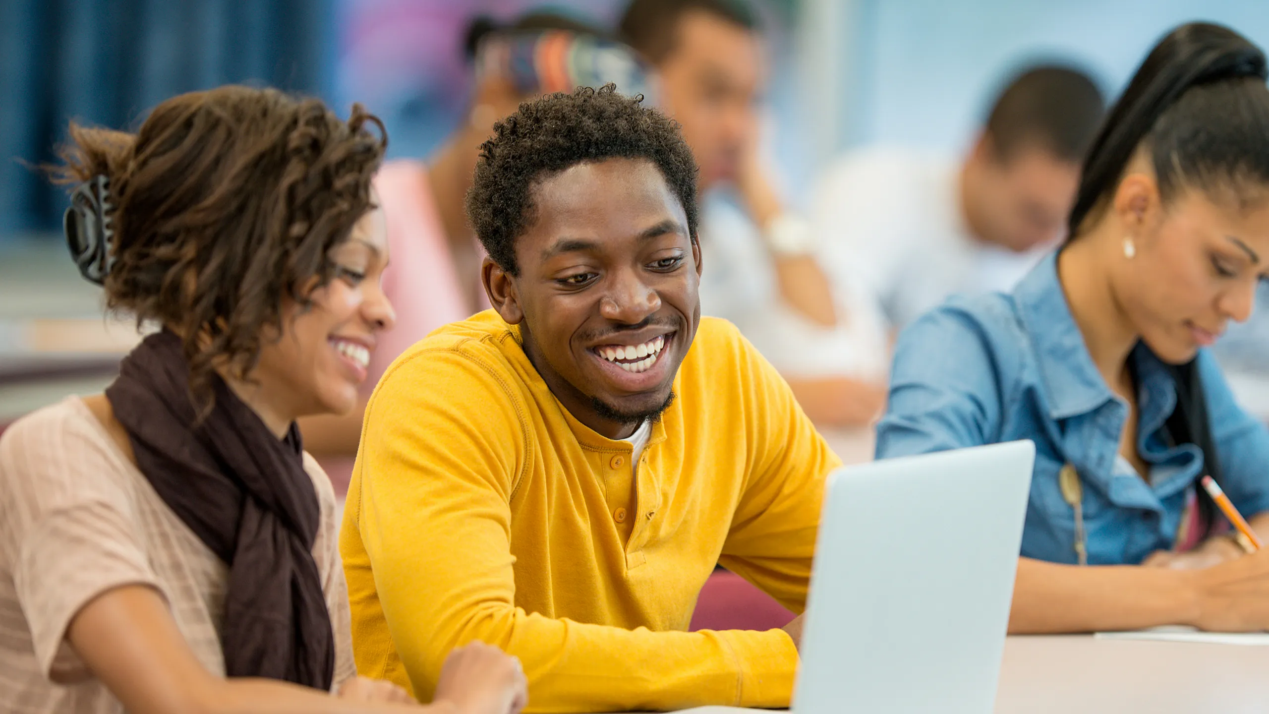 Diverse students enthusiastically collaborating on a laptop in a bright classroom setting.