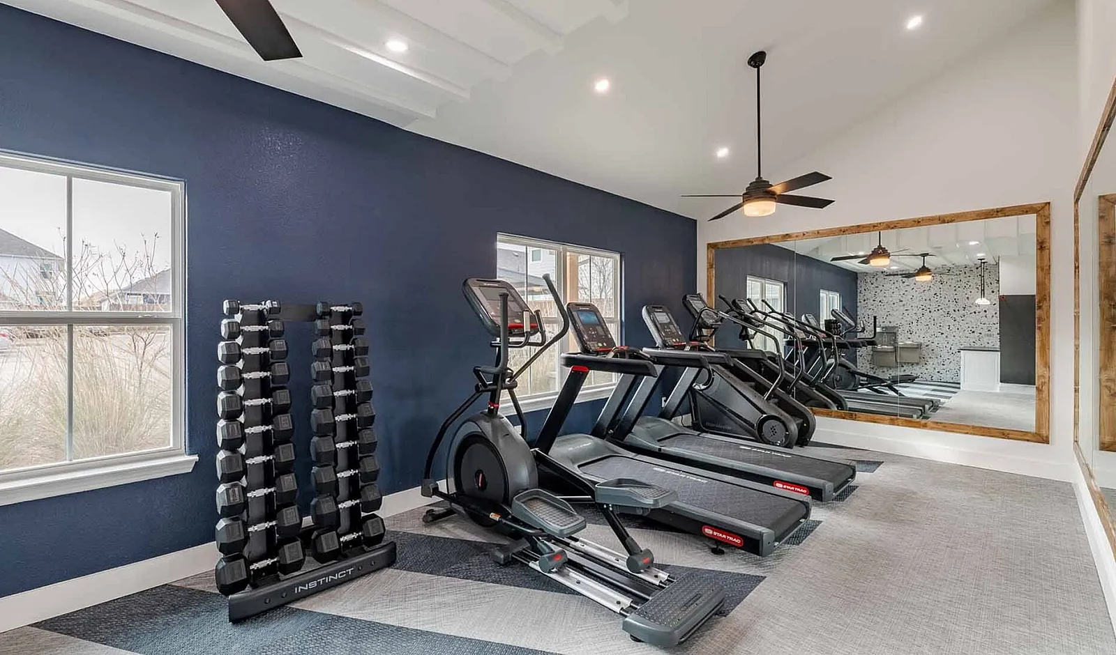 Modern fitness room with state-of-the-art treadmills, elliptical machine, and a neatly organized dumbbell rack, perfect for an energizing workout.