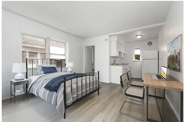 Bright studio apartment with a comfortable bed, modern kitchenette, and a sleek work desk.