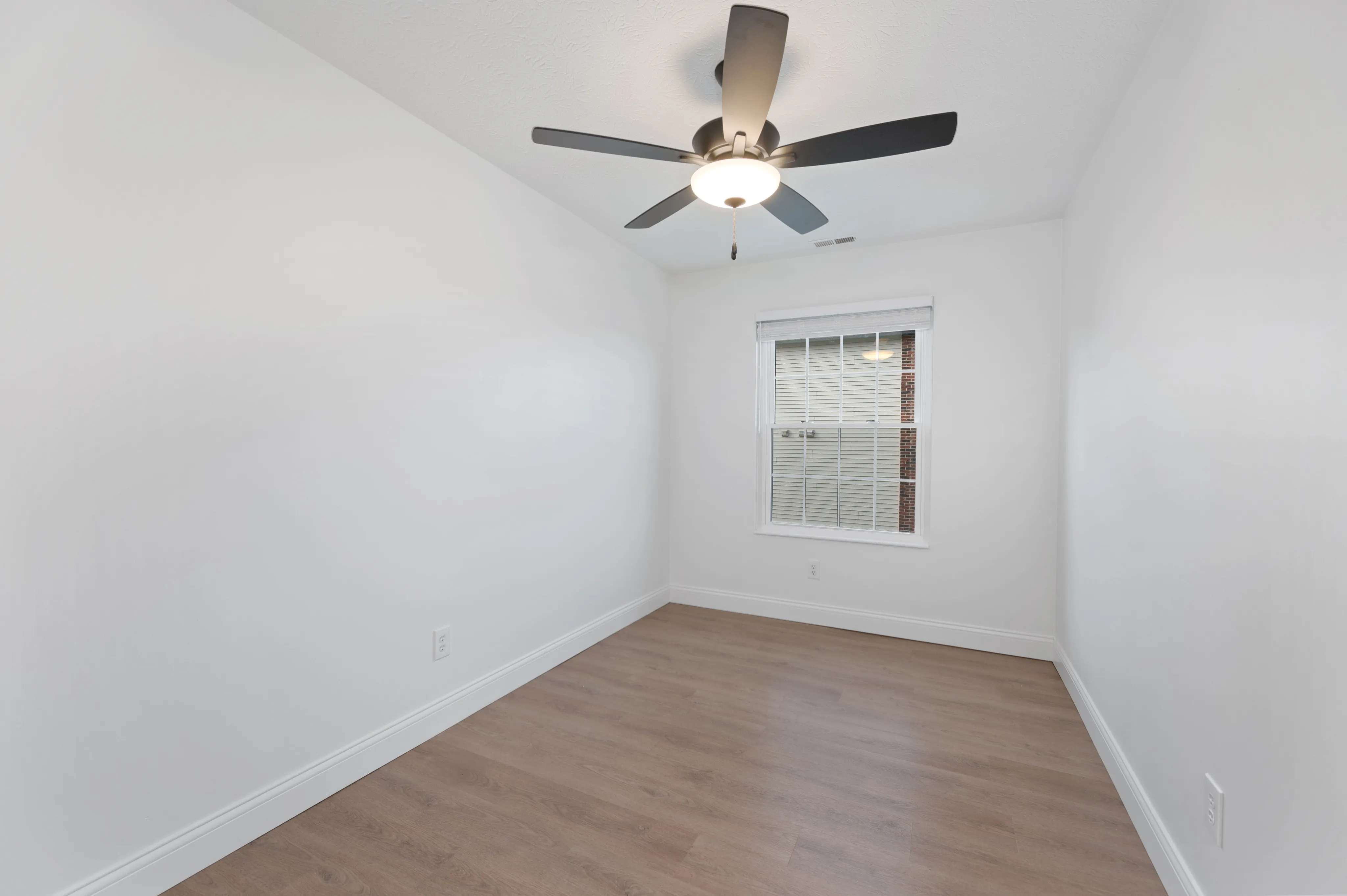 Elegant room with hardwood flooring, white walls, a ceiling fan, and a window offering natural light.