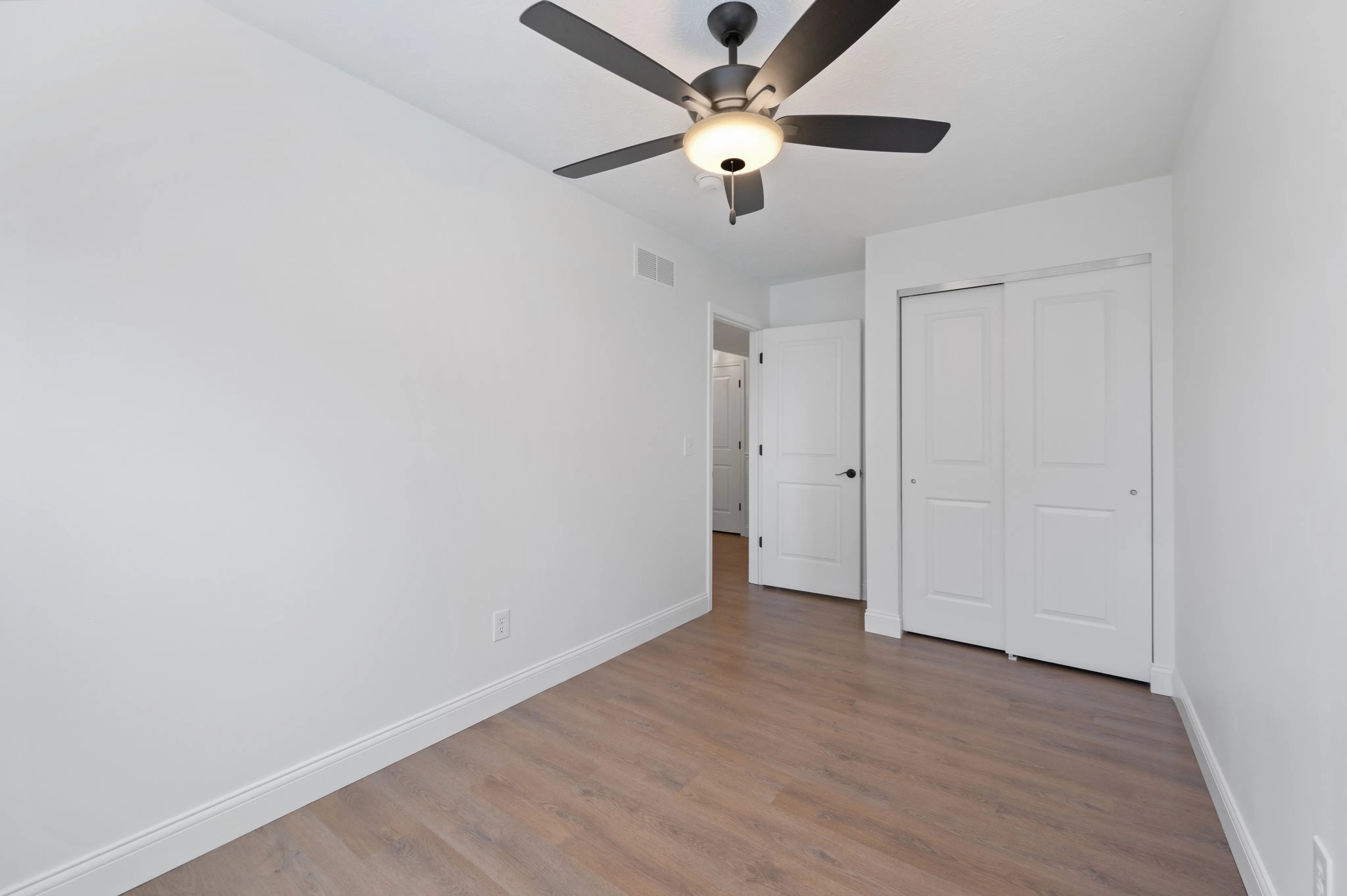 Bright bedroom with wooden flooring and modern ceiling fan.