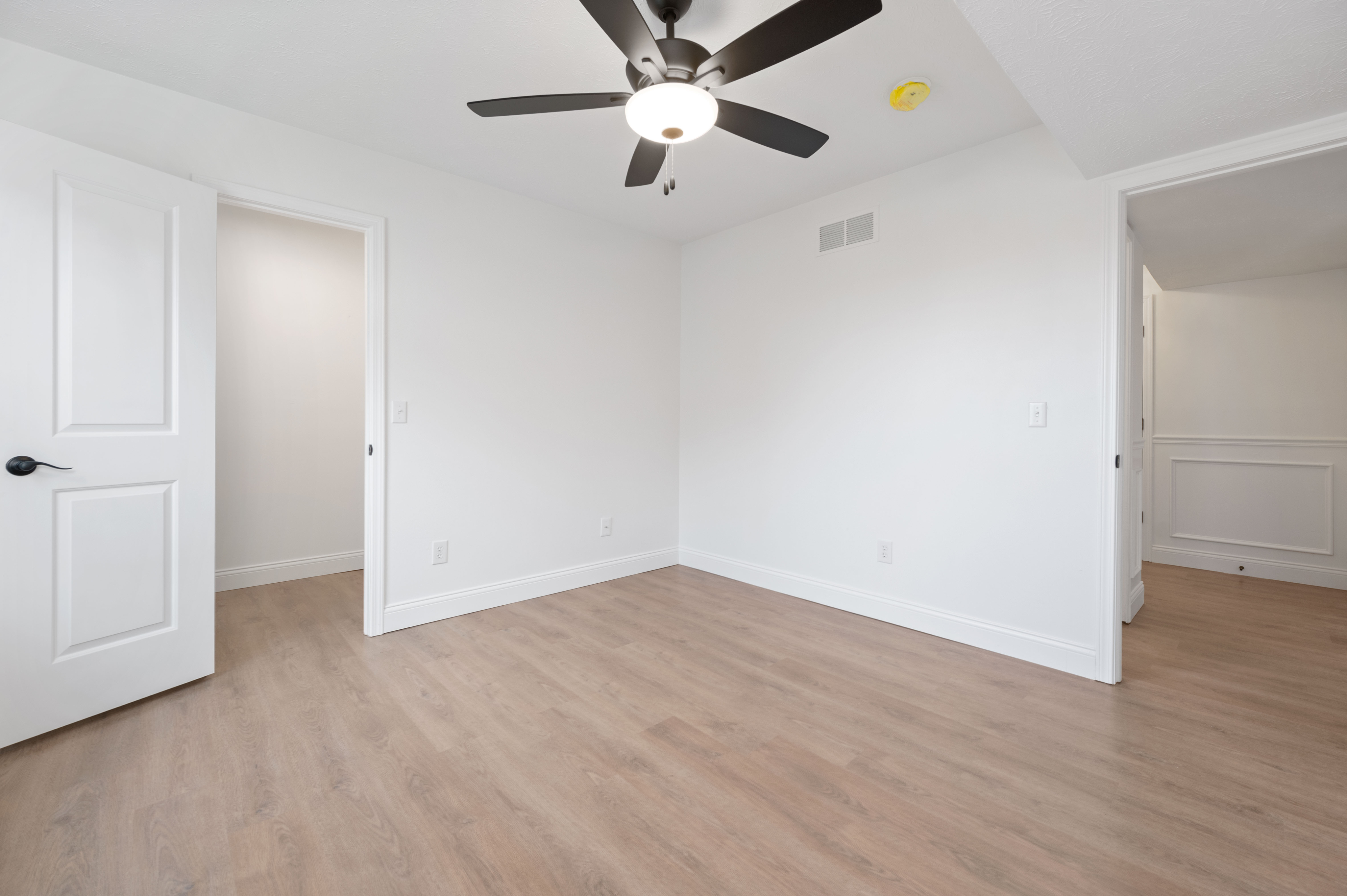 Modern empty bedroom with wooden floors and ceiling fan, perfect for customization.