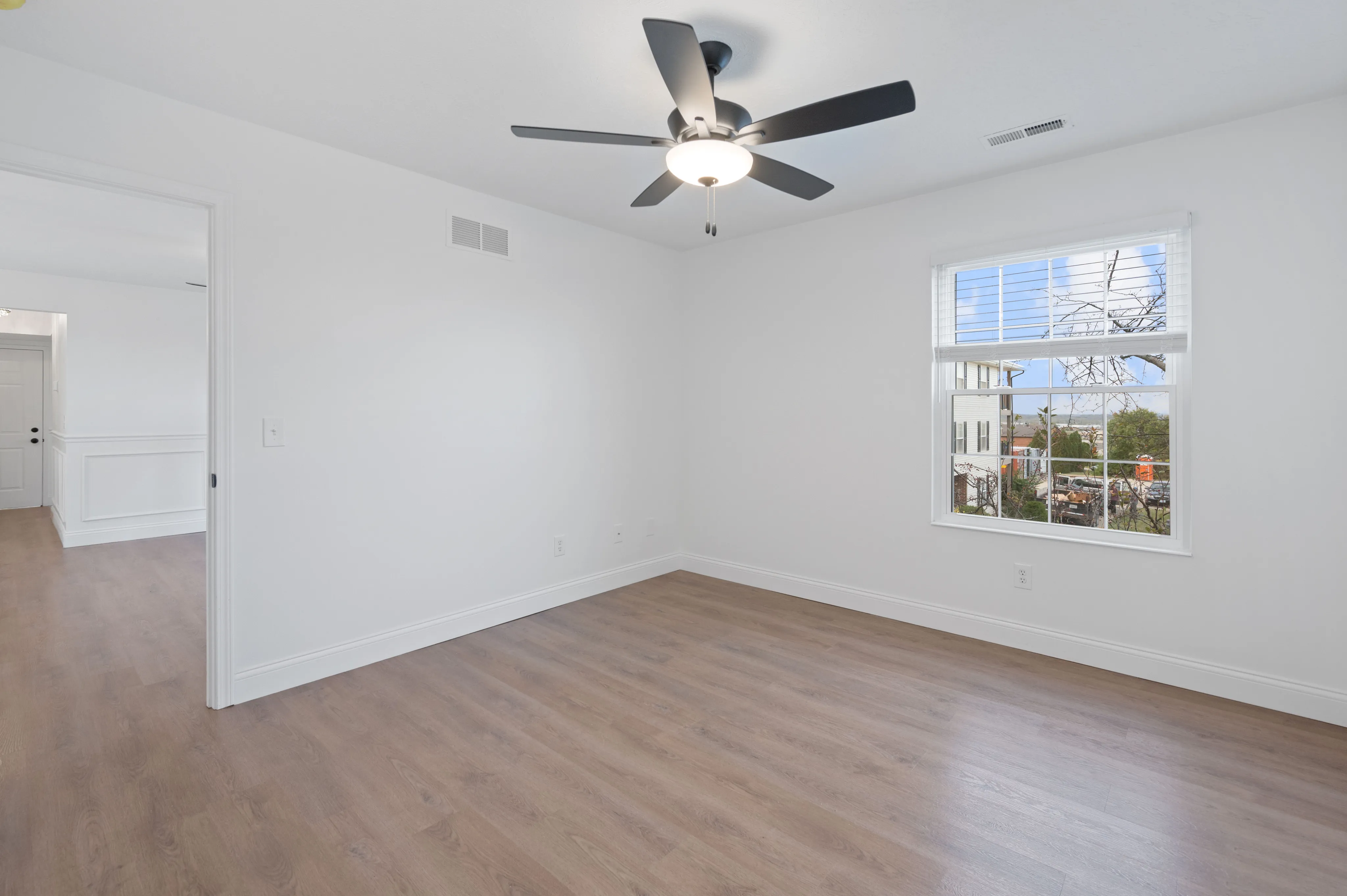 Spacious bedroom with wooden floors, large window, and modern ceiling fan.