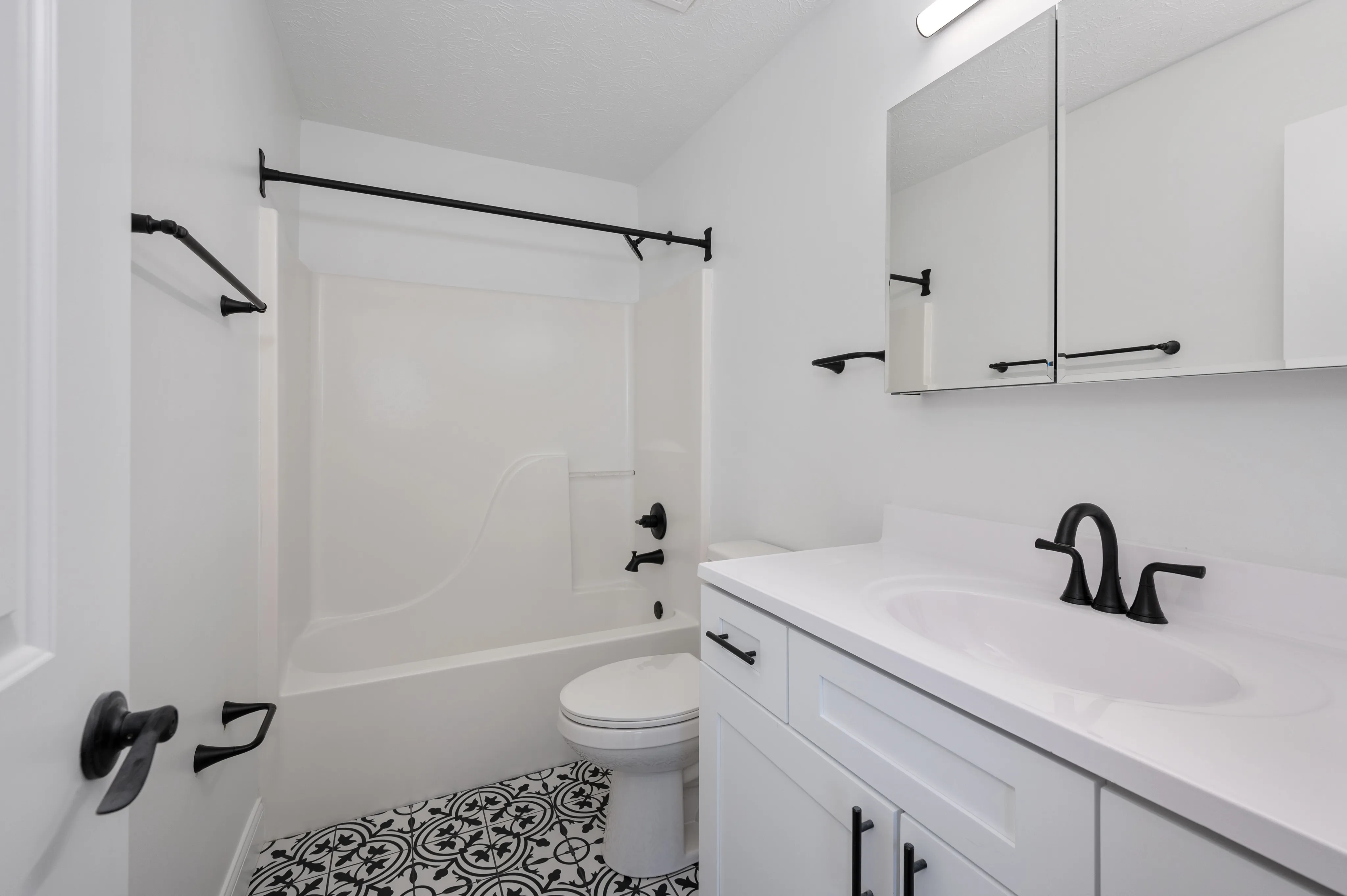 Modern bathroom with black fixtures, patterned tile floor, and sleek white vanity.