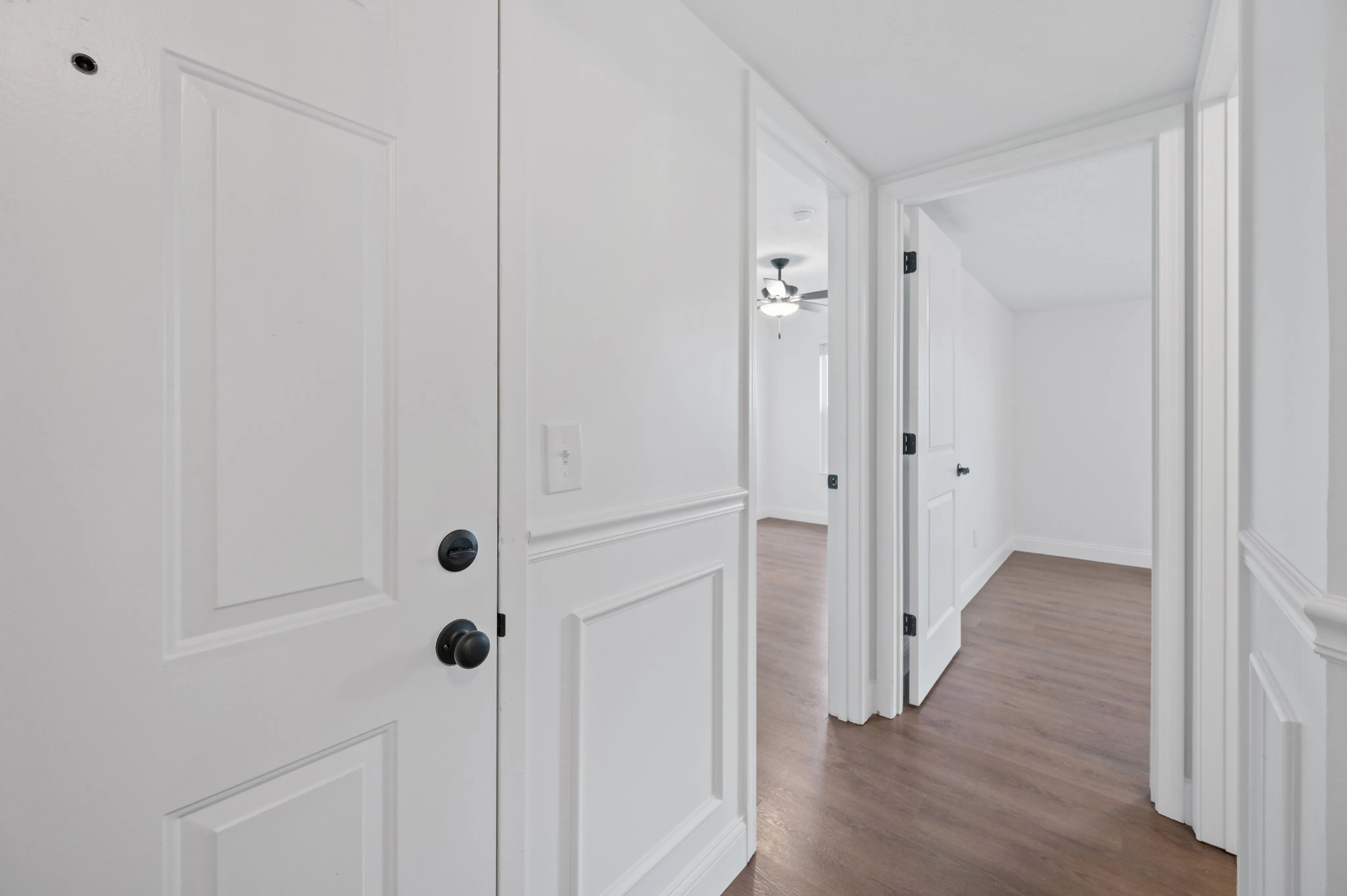 Inviting apartment entryway leading to a bright hallway with wooden flooring and modern white doors.