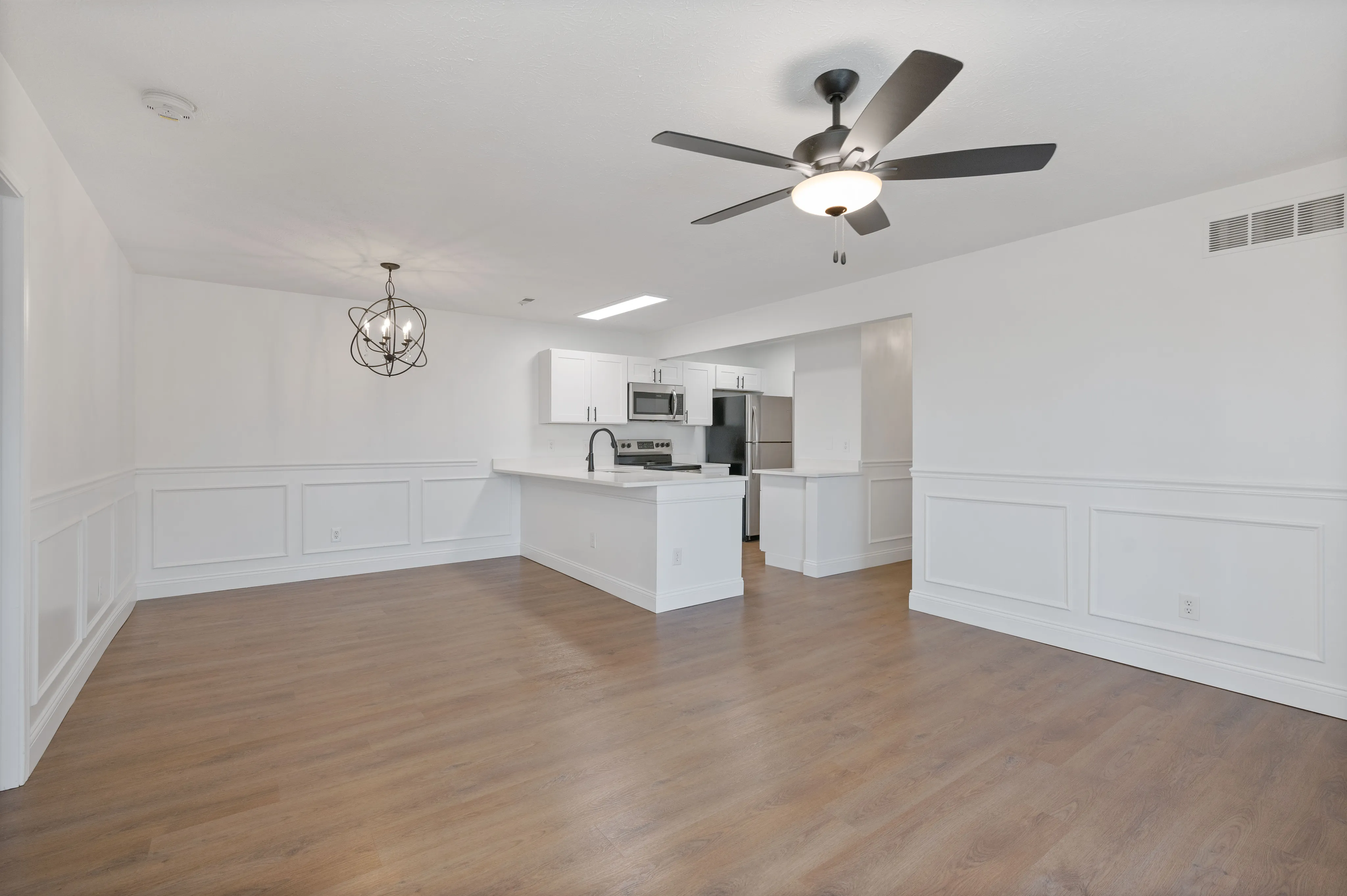 Modern open-concept kitchen with sleek white cabinets and a stylish dining area with a contemporary chandelier.