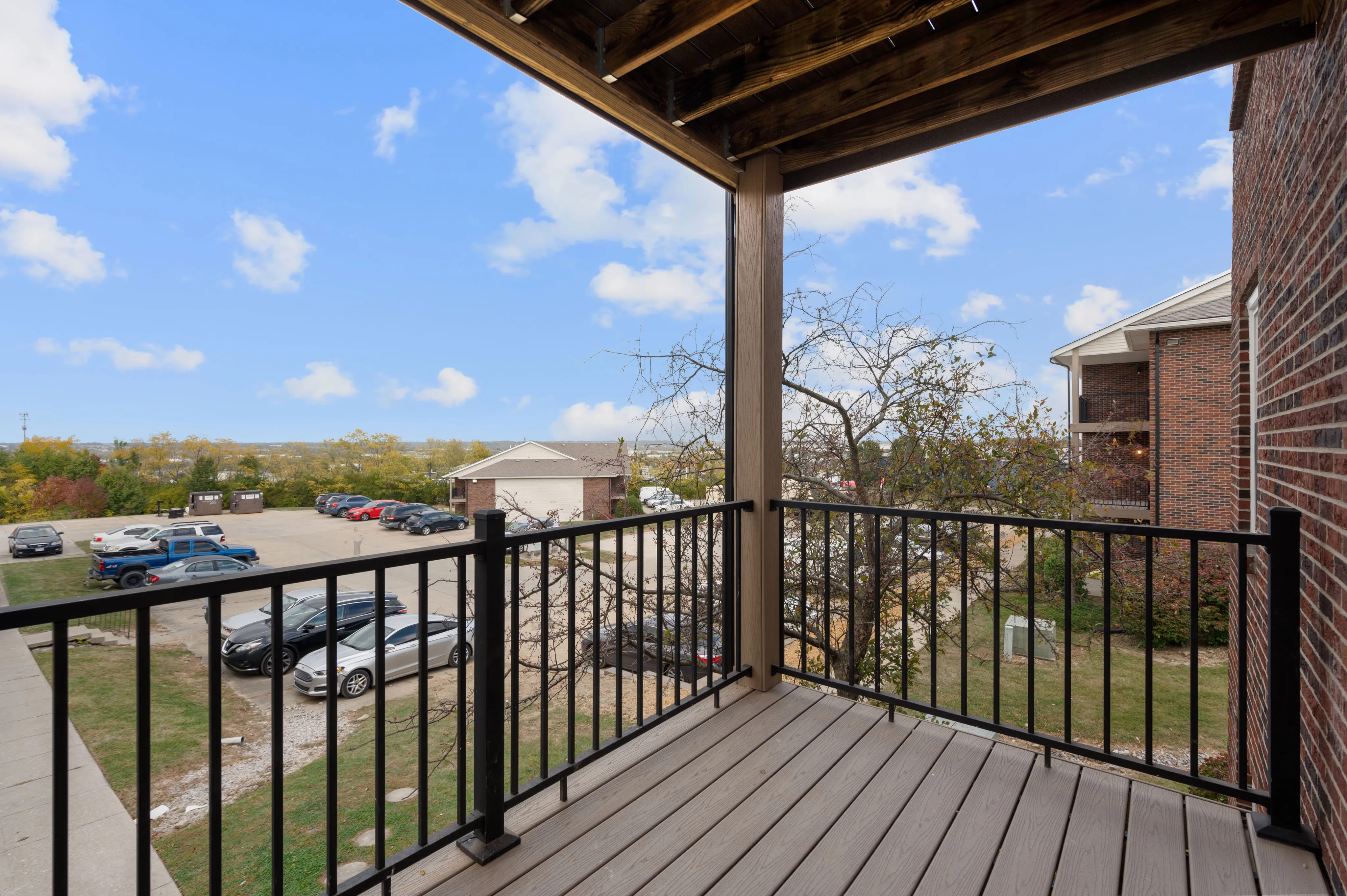 Inviting balcony overlooking a scenic parking area with trees and blue skies in a residential setting.